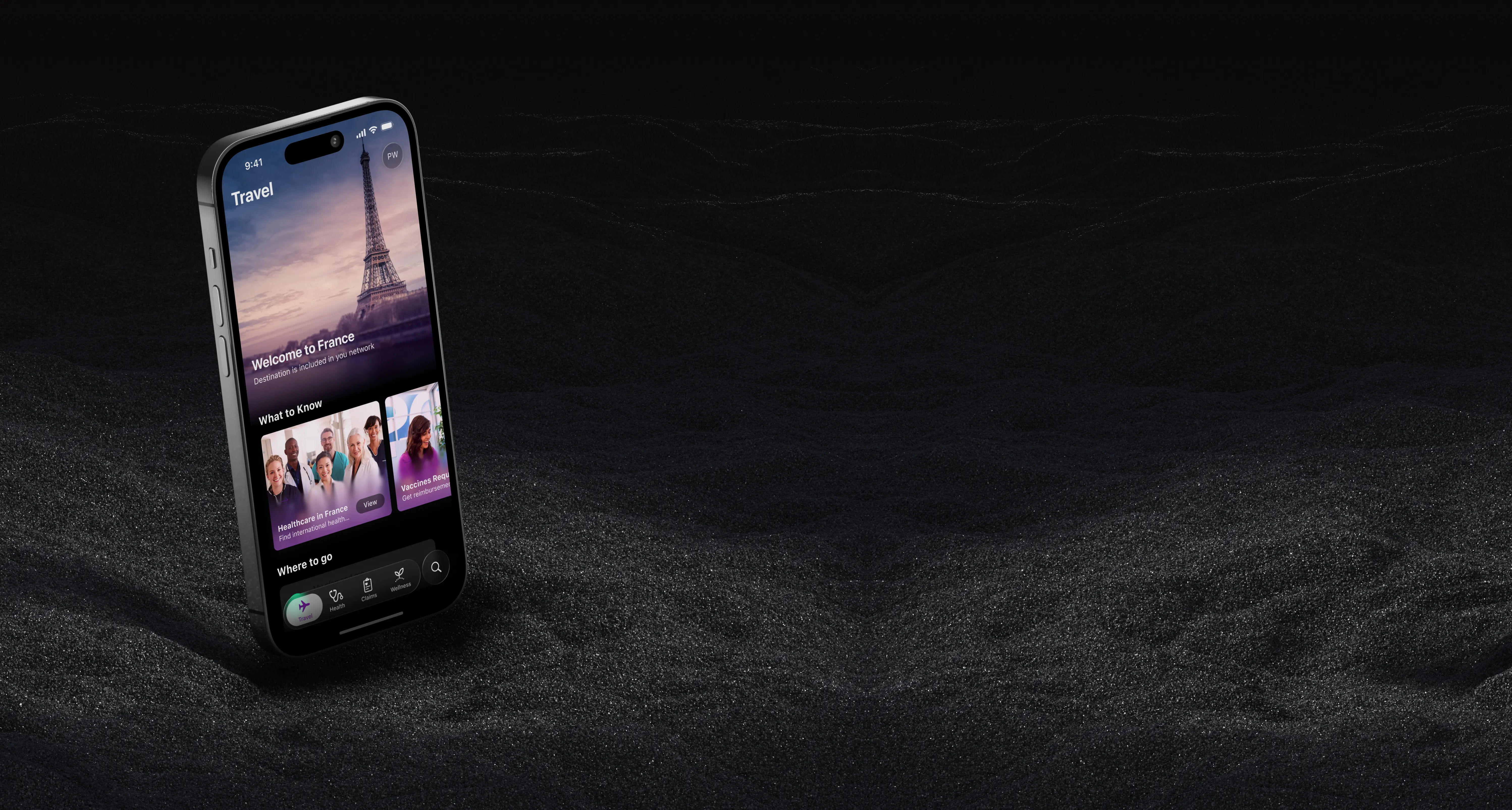 iPhone standing on dark sand, showing the Aetna travel screen with a photo of the Eiffel Tower and the heading Welcome to France